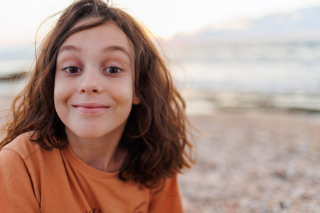 Portrait of a boy with long hair wearing an orange T-shirt outdoors.