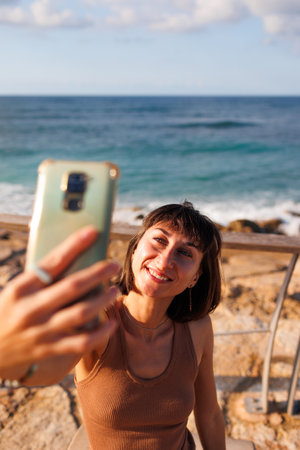 girl relaxes by the sea and takes a selfie. beautiful tourist takes a selfie on the embankment. travel and adventure.の写真素材
