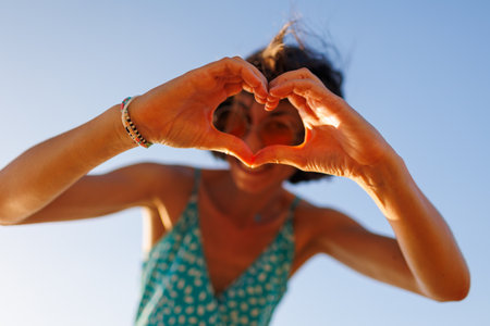 young girl makes a heart. a symbol of the shape of love. cheerful woman in orange sunglasses making a heart shape with her hands. girl having fun on the beach.の写真素材