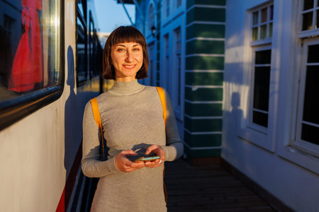 A young beautiful girl is waiting for the train and using the phone. Enjoying the trip. Travel concept.の写真素材