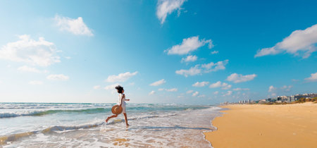 happy girl in a white dress runs along the beach and enjoys her vacation. A carefree girl walks along the beach on a sunny day. slender girl in a white dress on the beach.の写真素材