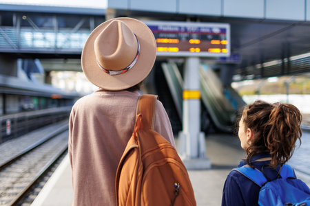 Mom and child with backpacks are waiting for the train on the platform. The family is ready to...