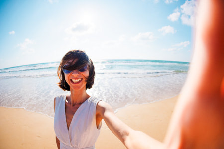 Photo of a surprised excited young beautiful girl walking on the beach and taking a selfie to the camera. girl takes a selfie.の写真素材