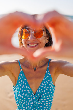 Close-up of a smiling woman making a heart shape with her hands. joyful woman laughs in front of the camera. girl has fun on the beach.の写真素材