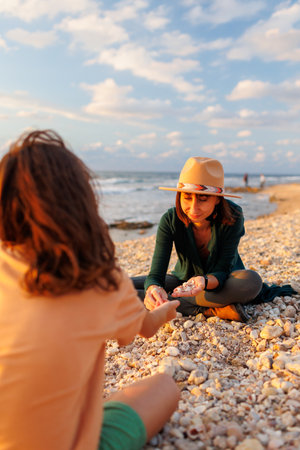 boy collects shells and pebbles in the sea on a sandy beach with his mother. Family having fun on the beach collecting shells. mother and sonの写真素材