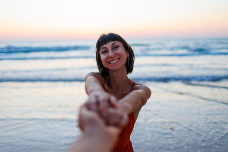happy young woman pulls guy's hand. a beautiful girl in a dress walks along the beach, holding a guy