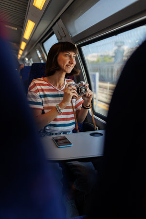 train travel. A young woman enjoys a train ride and takes pictures of beautiful tourist spots with her camera. film camera the girl uses a film camera.の写真素材