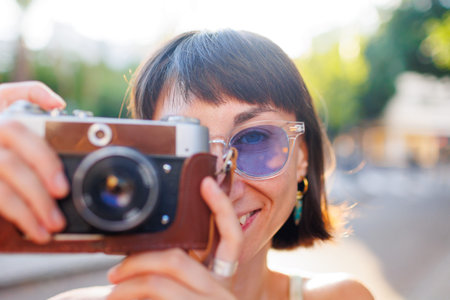 young girl in stylish clothes walks around the city and takes photographs with a film camera....
