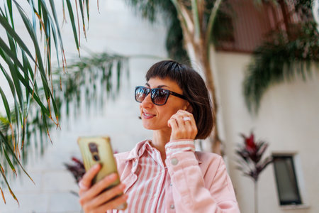 portrait of an elegant woman in stylish clothes with a smartphone on a city street. Happy business woman using phone and headphones outdoors. Successful business womanの写真素材