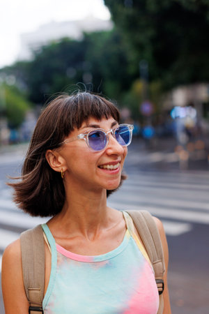 Portrait of a cheerful, joyful beautiful young woman with a sweet smile wearing fashionable clothes and sunglasses outdoors in the city on a bright sunny day. girl enjoying a walk in the city.の写真素材