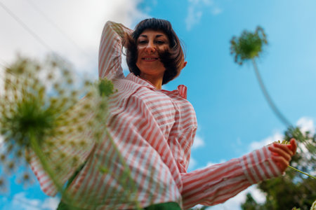 girl in a pink shirt moves in the blue sky. Portrait of a young girl enjoying nature outdoors in a field with flowers. The face of a young girl close-up.の写真素材