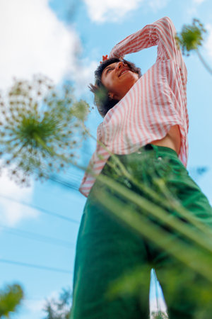 bright young girl in stylish clothes, wearing a pink shirt and green pants, poses against a background of blue sky and flowers. spring fashion.の写真素材