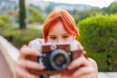 young girl takes photographs. teenager uses a camera on the street. girl with a camera.の写真素材