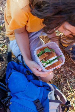 The boy is holding a lunchbox. The boy takes out a lunch box and prepares to eat on a hike. hiking...