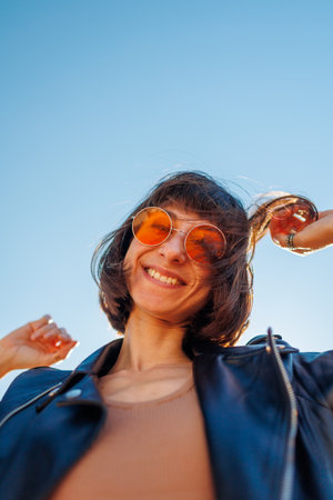 Girl dancing and enjoying music at a rock concert, stylish girl in a leather jacket dancing outdoors, happy woman in sunglasses.の写真素材