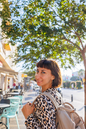 woman walking with a backpack around the city. walk around the city. a young cheerful woman in a...