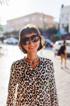 girl in stylish clothes walks around the city. young cheerful woman in leopard blouse walks down the...