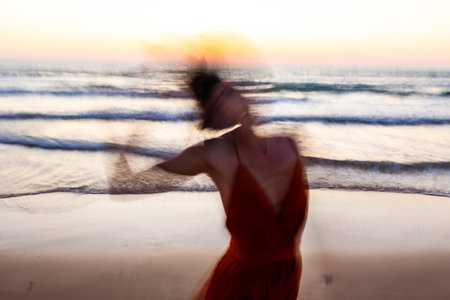 Happy woman in a red dress walks along the beach. soft focus and long shutter speed. Blurred motion. Summer mood.の写真素材