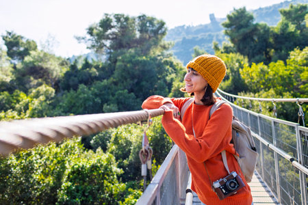 Travel and photography. A young woman with a camera and a backpack walks along a suspension bridge....