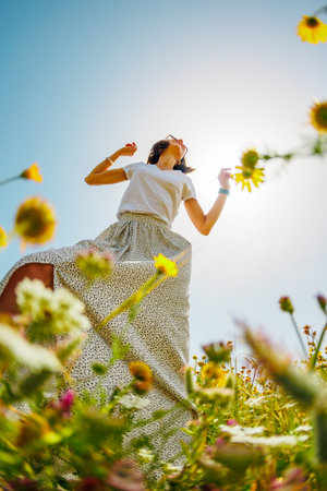 Summer mood. a young and cheerful girl posing against a background of blue sky and flowers. A beautiful girl dances among flowers. Happy girl among blooming flowers, outdoors. spring fashion.の写真素材