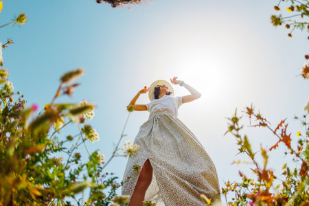 Summer mood. a young and cheerful girl posing against a background of blue sky and flowers. A beautiful girl dances among flowers. girl dancing among flowers. spring fashion.の写真素材