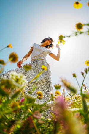 Summer mood. a young and cheerful girl posing against a background of blue sky and flowers. girl dancing among flowers. spring fashion.の写真素材