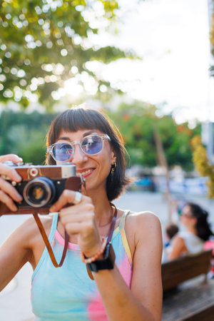 young girl in stylish clothes walks around the city and takes photographs with a film camera....