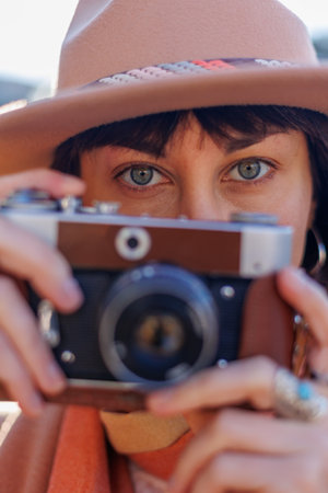 Fashionable look, young woman with a film camera wearing an elegant hat and coat. A hipster tourist woman holds a camera in her hands and takes a photo. film cameraの写真素材