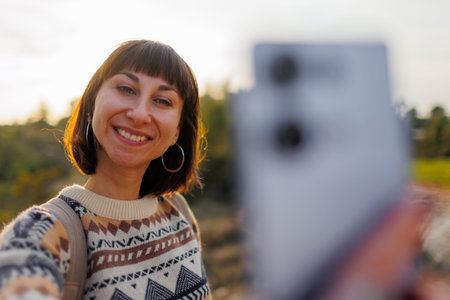 Young female traveler taking a selfie portrait at sunset. Happy smiling girl using smartphone....