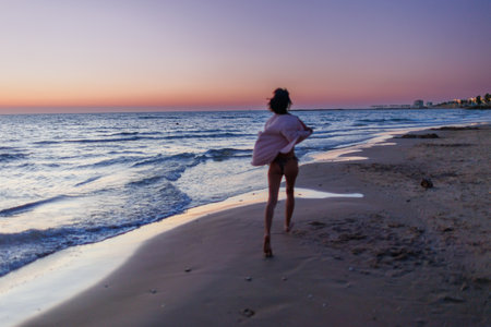 summer mood. a young girl in a shirt runs along the beach barefoot at sunset. girl having fun on the beach.の写真素材