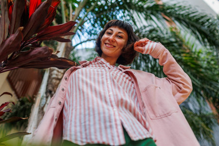 Close-up portrait of a broadly smiling girl. The girl wears a pink shirt. Elegant carefree girl having fun in the park. Emotional brunette enjoying sunny days.の写真素材