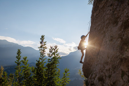 climber boy the child trains in rock climbing. sports in nature. cute teen kid climbing on rock with insurance, lifestyle sport people conceptの写真素材