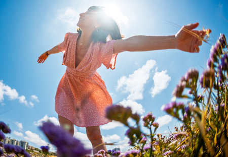 Beautiful woman in a flower field raising her hands and enjoying the moment. summer mood. slender girl in a summer dress. girl on a background of flowers.の写真素材