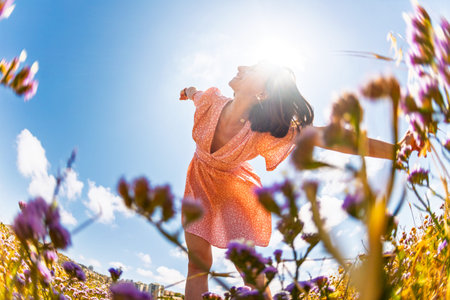 Beautiful woman in a flower field raising her hands and enjoying the moment. summer mood. slender...