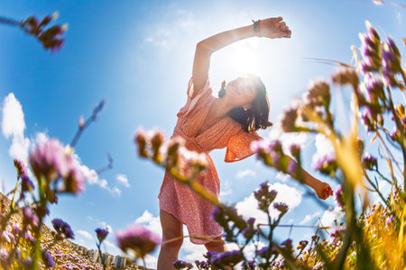 Beautiful woman in a flower field raising her hands and enjoying the moment. summer mood. slender girl in a summer dress. girl on a background of flowers.の写真素材
