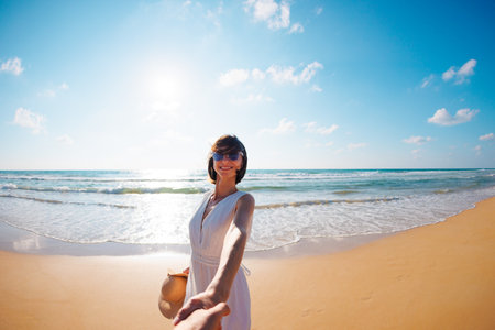 couple in love having fun on the beach. Follow me. happy young woman pulling guys hand. a beautiful girl in a dress walks along the beach, holding a guys hand, a romantic walk. Valentines Day.の写真素材