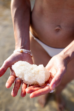 girl holds salt crystals in hand. female hand holds natural salt crystals on salty sea background. White natural salt. natural resources concept. dead sea. israel.の写真素材