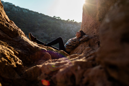 happy woman in the mountains. girl resting sitting on a stone in the mountains. trekking and hiking. concept of sports and healthy lifestyle. girl with a backpack.の写真素材