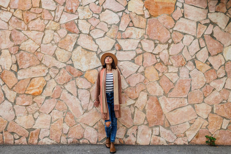 Portrait of a beautiful smiling model wearing a hat and stylish clothes against the background of a city wall. A woman poses near a wall on the street. Funny and positive woman having fun outdoors.の写真素材