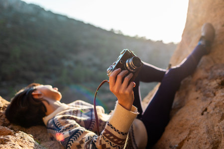 happy woman in the mountains with a camera in her hands. girl relaxing and taking photos in the mountains. trekking and hiking. girl with a camera. film cameraの写真素材