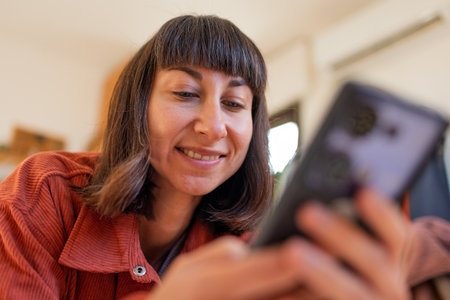Happy young girl relaxing at home on comfortable sofa, sending text messages on smartphone, smiling girl using mobile phone, shopping online from home.の写真素材