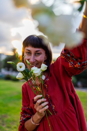 Romantic mood. Portrait of a young beautiful woman in a beautiful dress and with a bouquet of flowers at sunset. The girl smiles and looks at the camera.の写真素材
