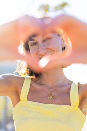 Close-up of young woman's hands making heart shape with fingers. Portrait of beautiful young woman...