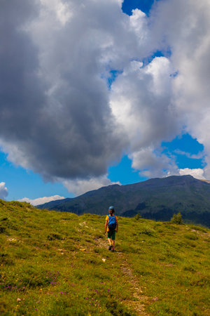 hiking in the mountains. A little boy with a backpack walks along a path against a backdrop of mountains with his back to the camera. trekking with a child.の写真素材