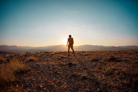 hiking in the mountains. a man with a backpack stands on a mountain against the backdrop of sunset. An active young man feels free. Travel to the mountains.の写真素材