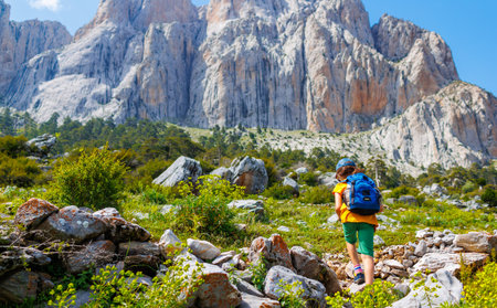 hiking in the mountains. A little boy with a backpack walks along a path against a background of mountains and clouds. Active healthy lifestyle on weekend hike journey. The concept of travelの写真素材
