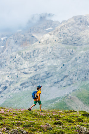 hiking in the mountains. A little boy with a backpack walks along a path against a background of mountains and clouds. Active healthy lifestyle on weekend hike journey. The concept of travelの写真素材