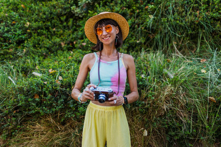 Stylish woman with a camera on the street. Portrait of a beautiful girl smiling on the street. Stylish tourist with a film camera. Girl with a camera.の写真素材