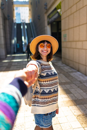 girls and her friend are walking in the city, a happy young woman holding a guy's hand and smiling...