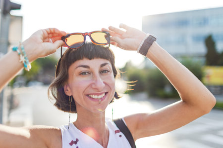 Beautiful brunette walking along sunny city street, urban style, smiling, summer trend.